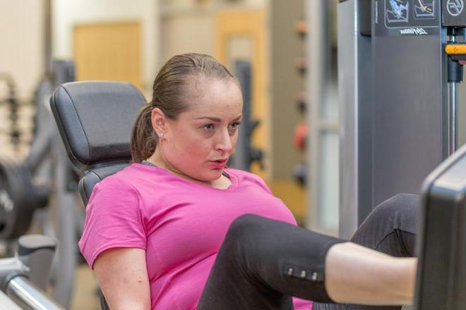 A woman sitting on and using a leg press exercise machine